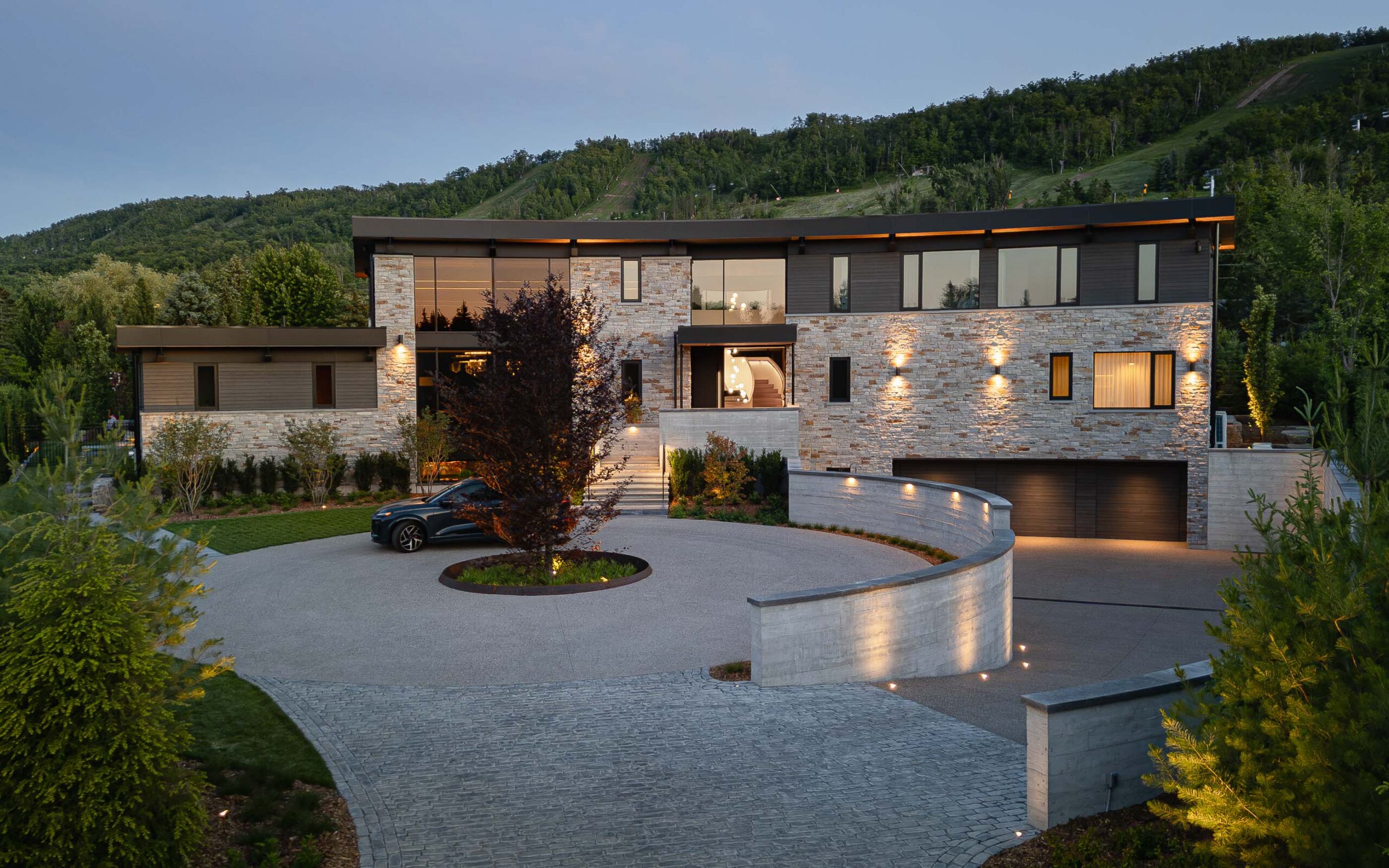 Driveway approach view of a luxury Blue Mountain chalet with distinctive curved architecture lit up at dusk