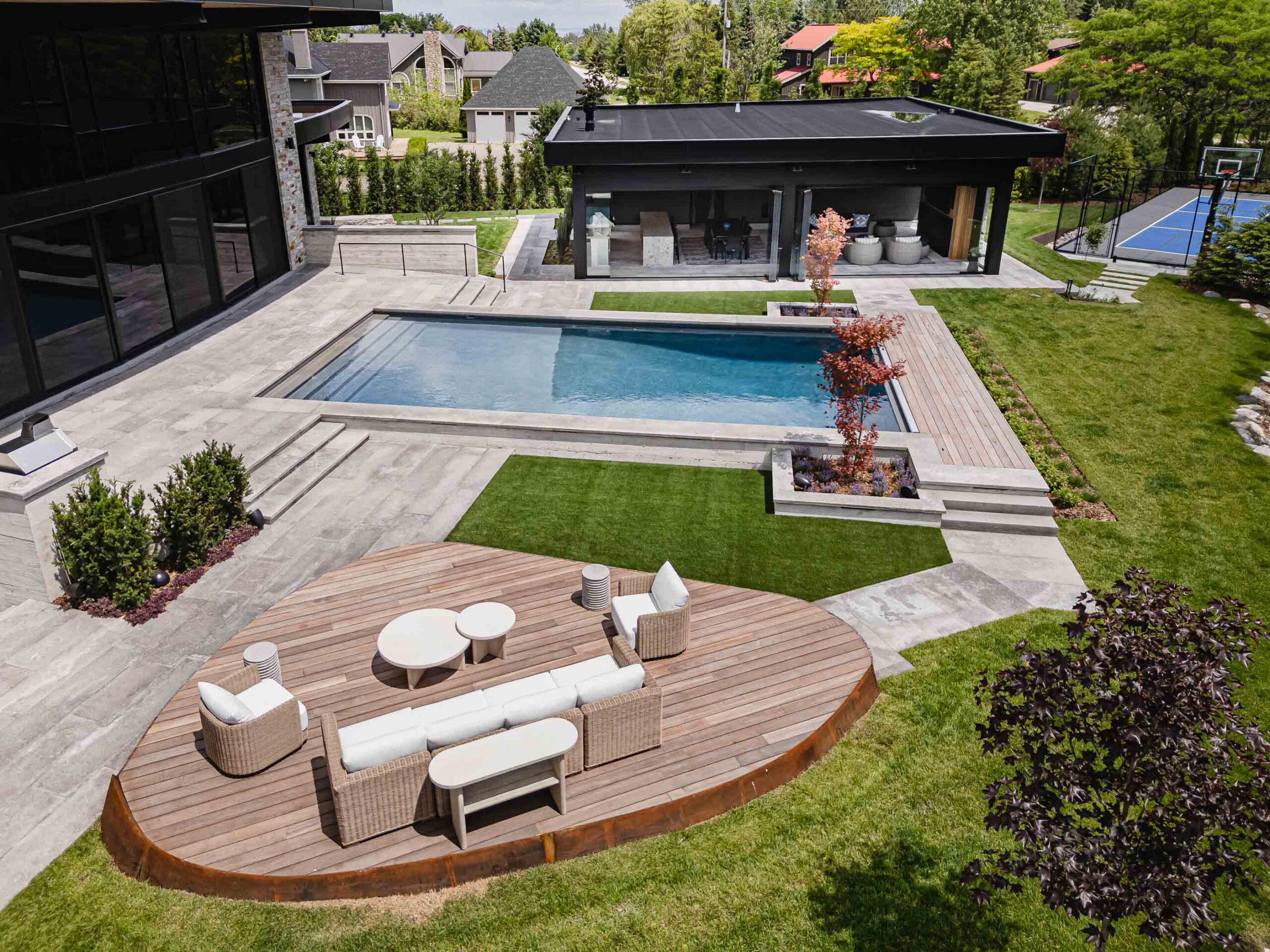 Aerial view of a custom, luxury chalet with pool, pool house with retractable glass walls, and elevated outdoor seating area