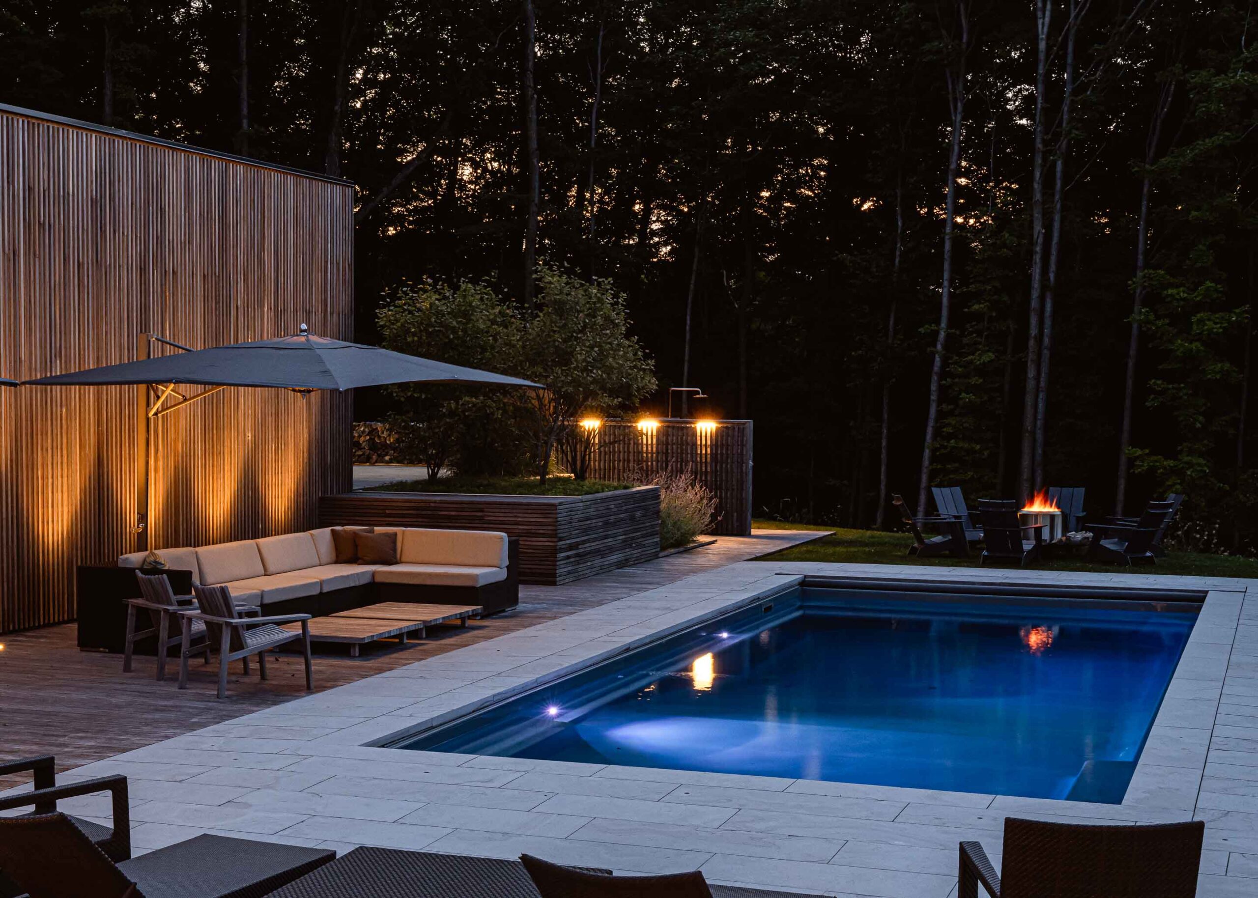 a modern pool lit up at night with vertical columns of light shining up a slat wall