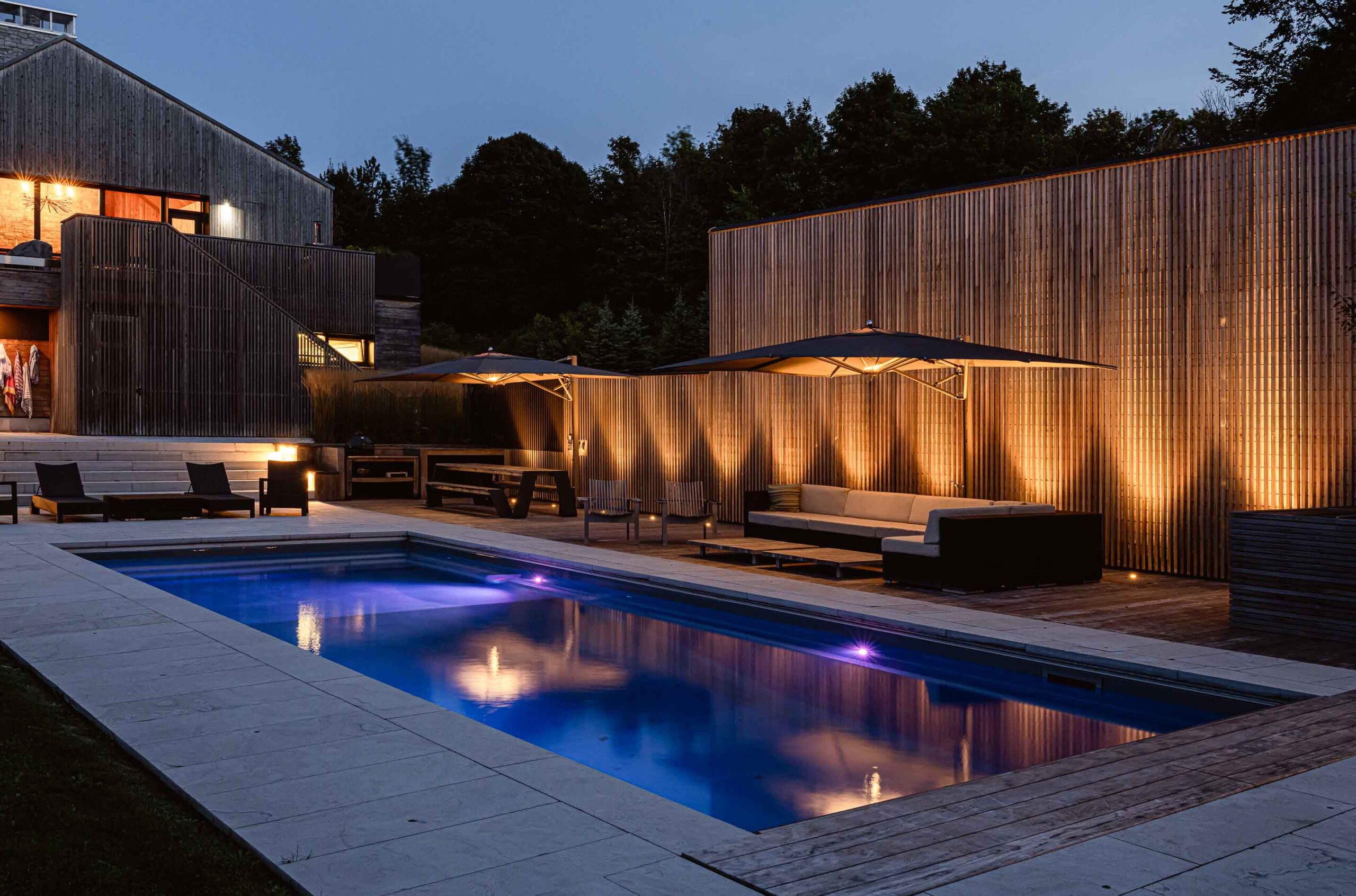 a modern pool lit up at night with vertical columns of light shining up a slat wall