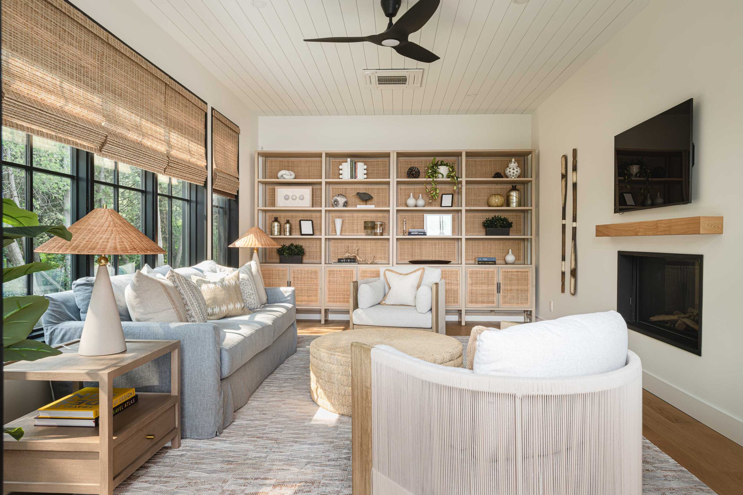 Sunroom in a modern beach house with shiplap ceiling, black framed windows, and contemporary fireplace