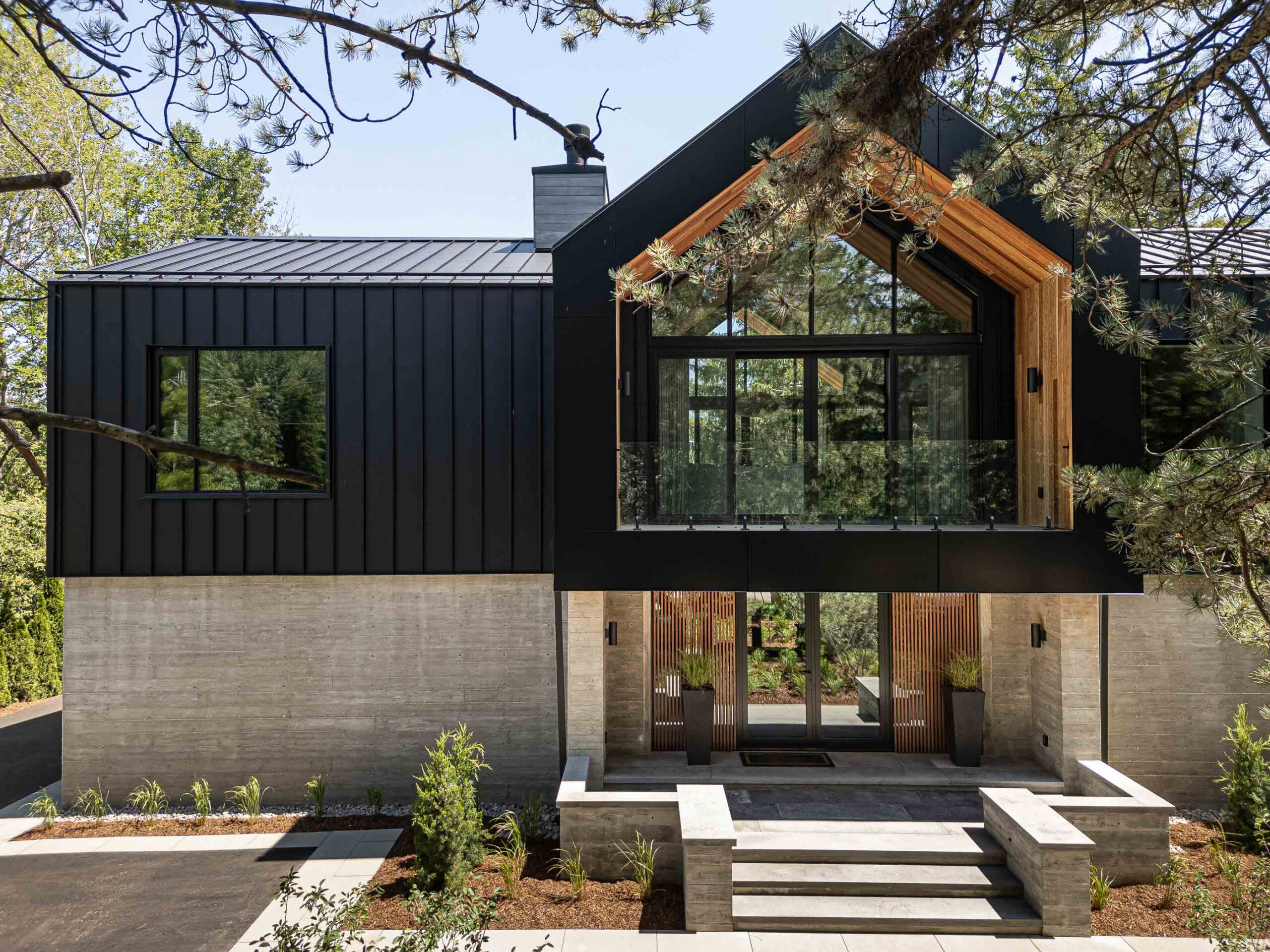 Front elevation of a Nordic-inspired Blue Mountain custom built chalet with expansive windows, board formed concrete and black metal siding