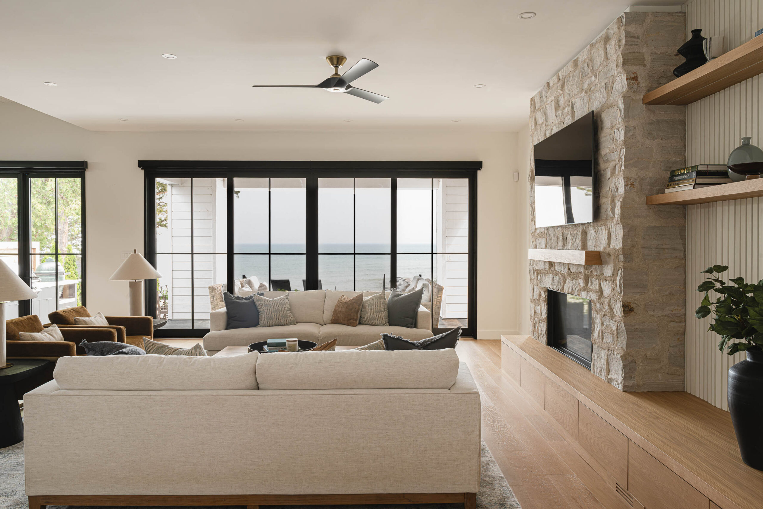 Living room of a modern beach house with natural stone fireplace, modern black framed patio doors overlooking Georgian Bay