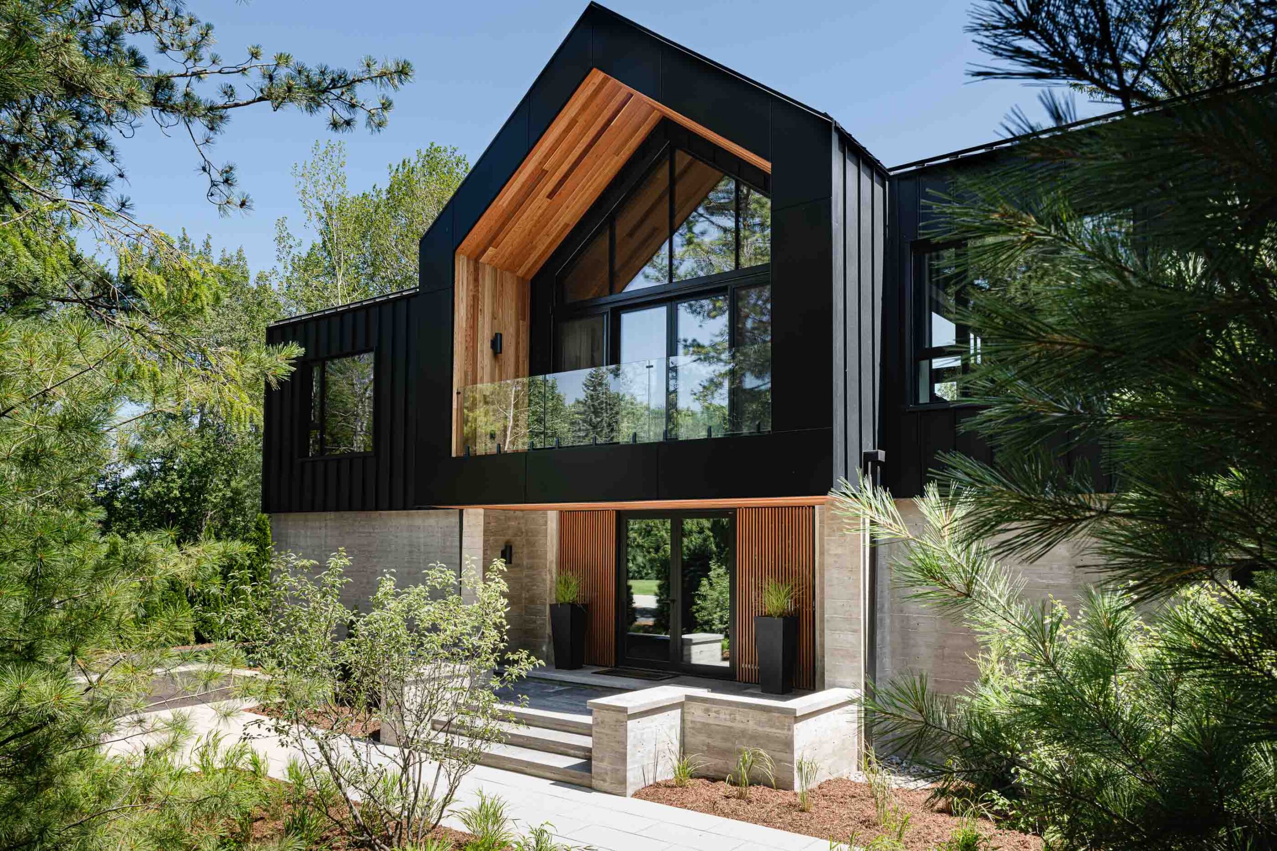 Front elevation of a Nordic-inspired Blue Mountain custom built chalet with expansive windows, board formed concrete and black metal siding
