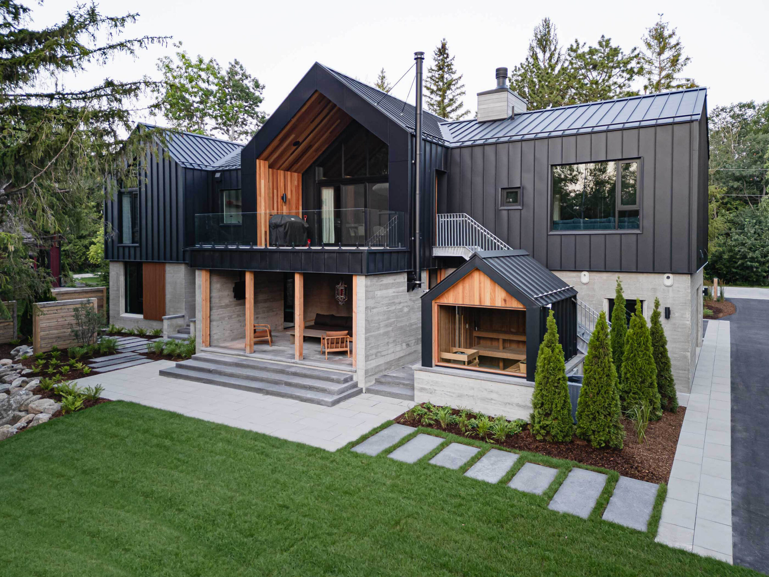 Contemporary Blue Mountain chalet with board formed concrete, black metal siding, screened outdoor seating area, and attached sauna