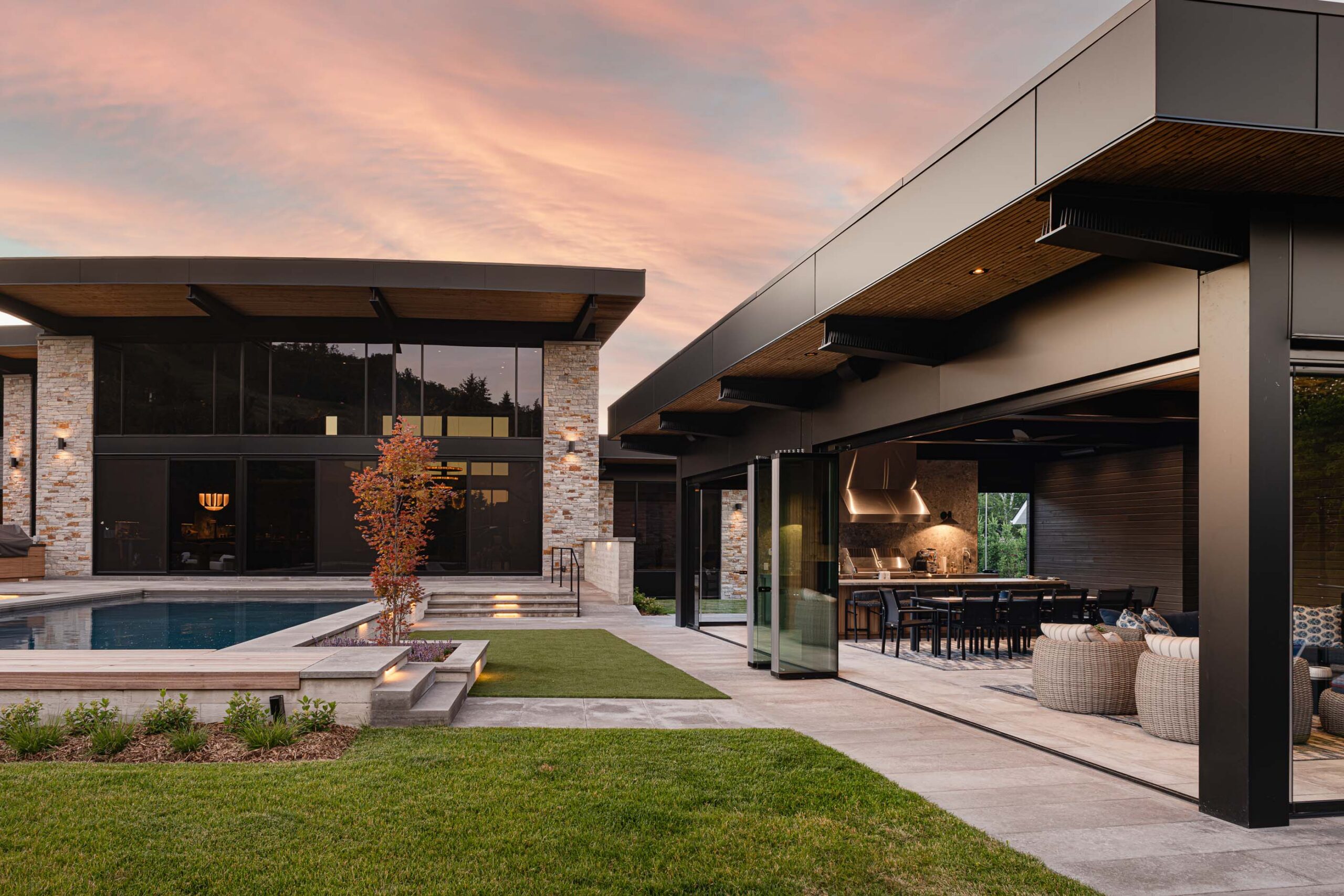 Modern pool house captured at dusk, with retractable glass wall open to reveal the kitchen, dining and living areas