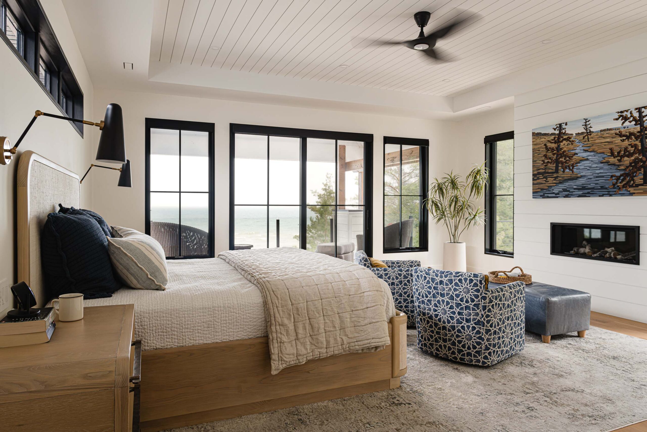Primary bedroom of a modern beach house with views of Georgian Bay, shiplap detailing and modern black framed windows and patio doors leading to a private balcony