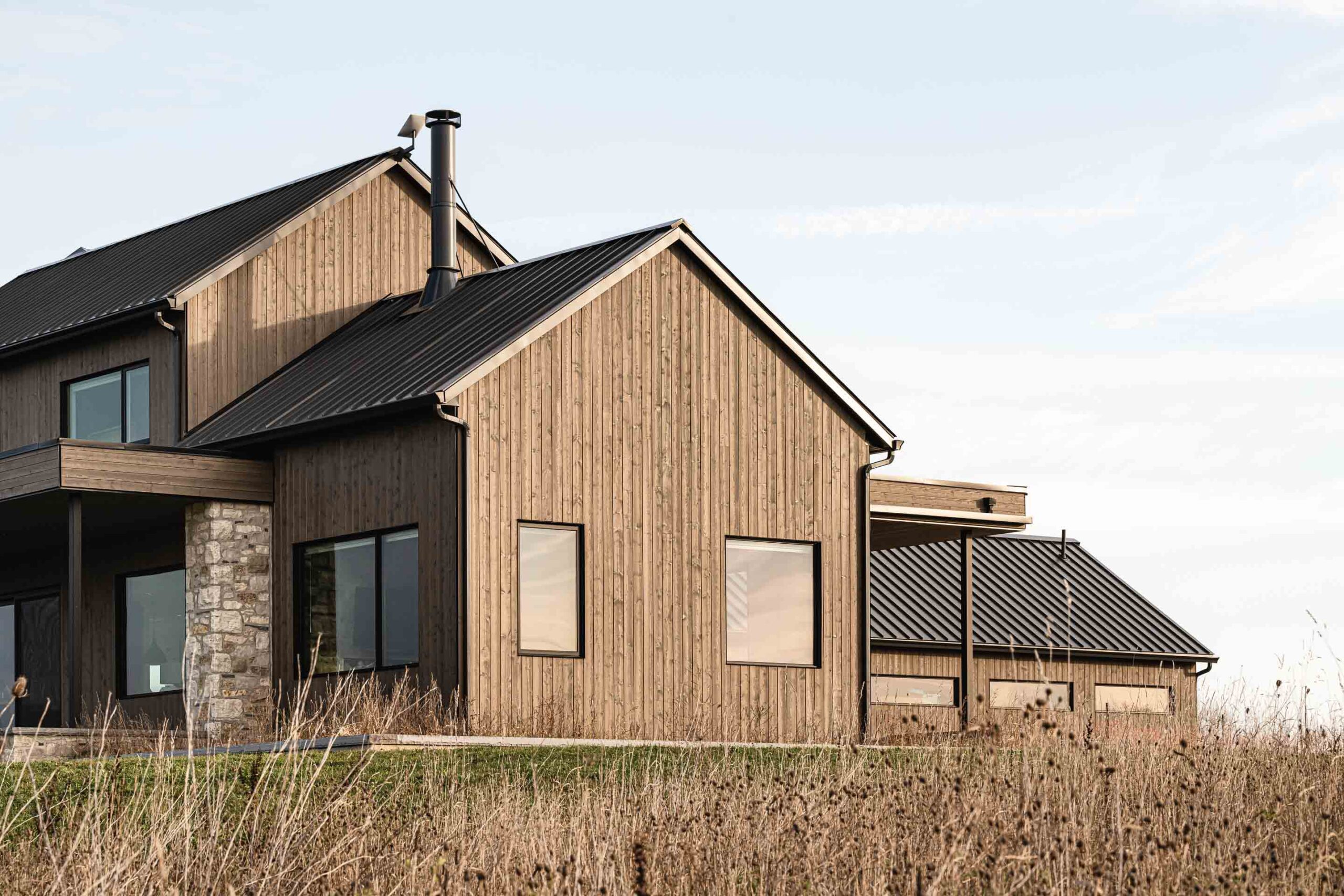 Warm light hits the exterior of a contemporary farmhouse with rich, wood siding and modern lines