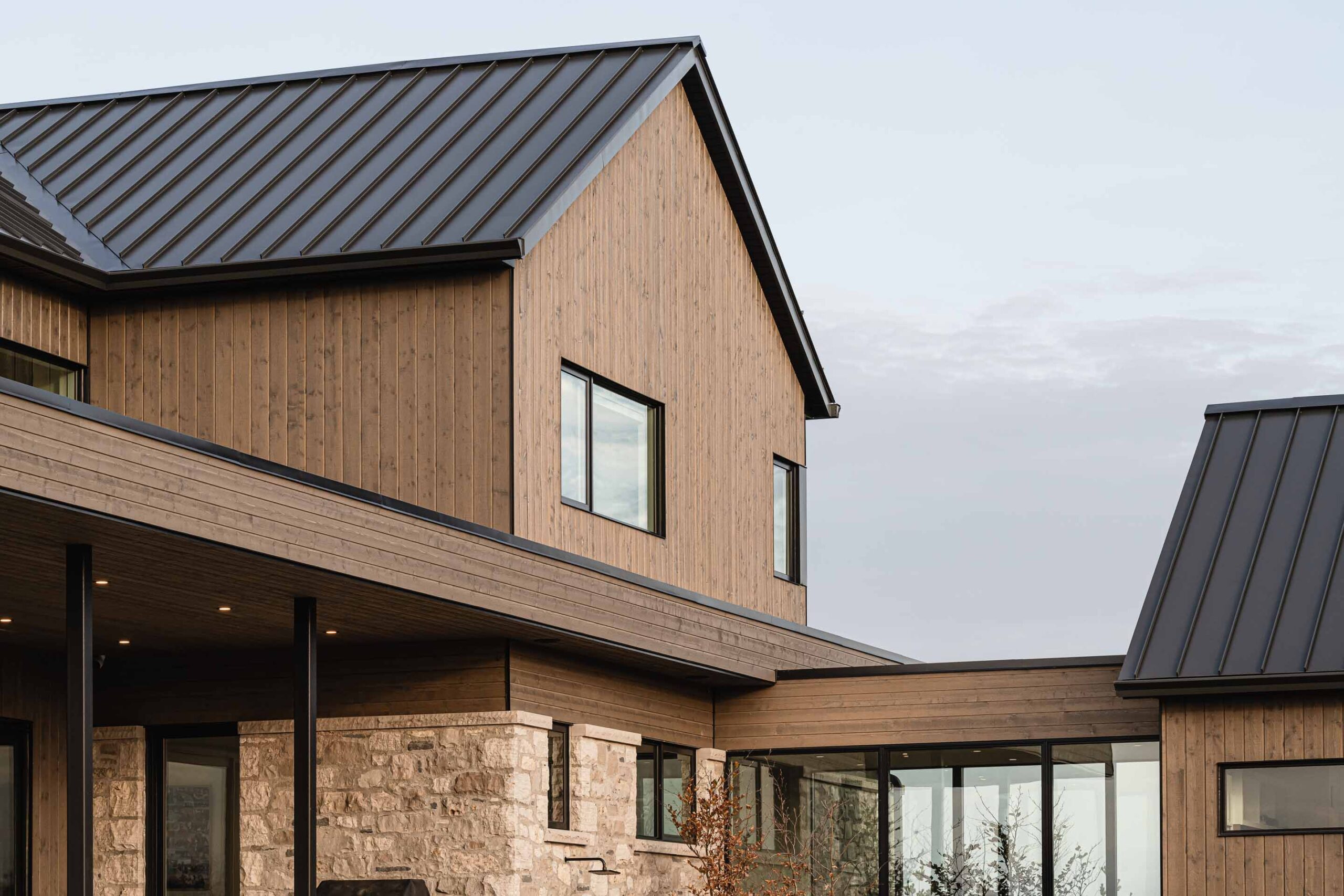 Architectural detail of a contemporary country home, featuring stone, wood and metal materials, a glass breezeway, and modern lines