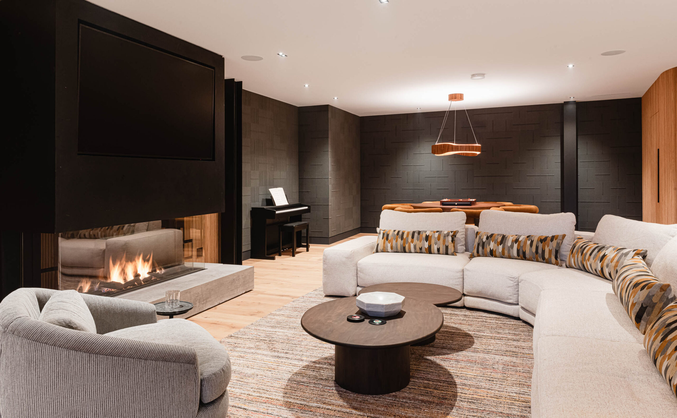 Contemporary Blue Moutnain chalet rec room with textured wallpaper, fluted wood paneling, and a glass, concrete and metal fireplace with integrated TV