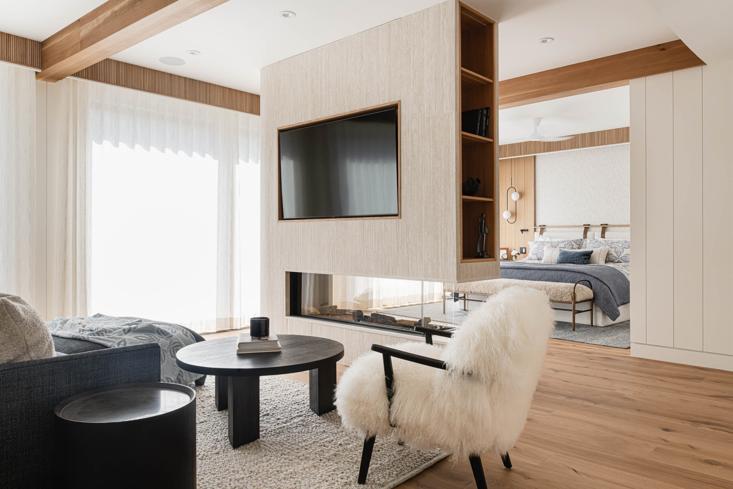 Contemporary primary bedroom with floor-to-ceiling windows, custom upholstered headboard wall, and curved tile and glass double-sided fireplace