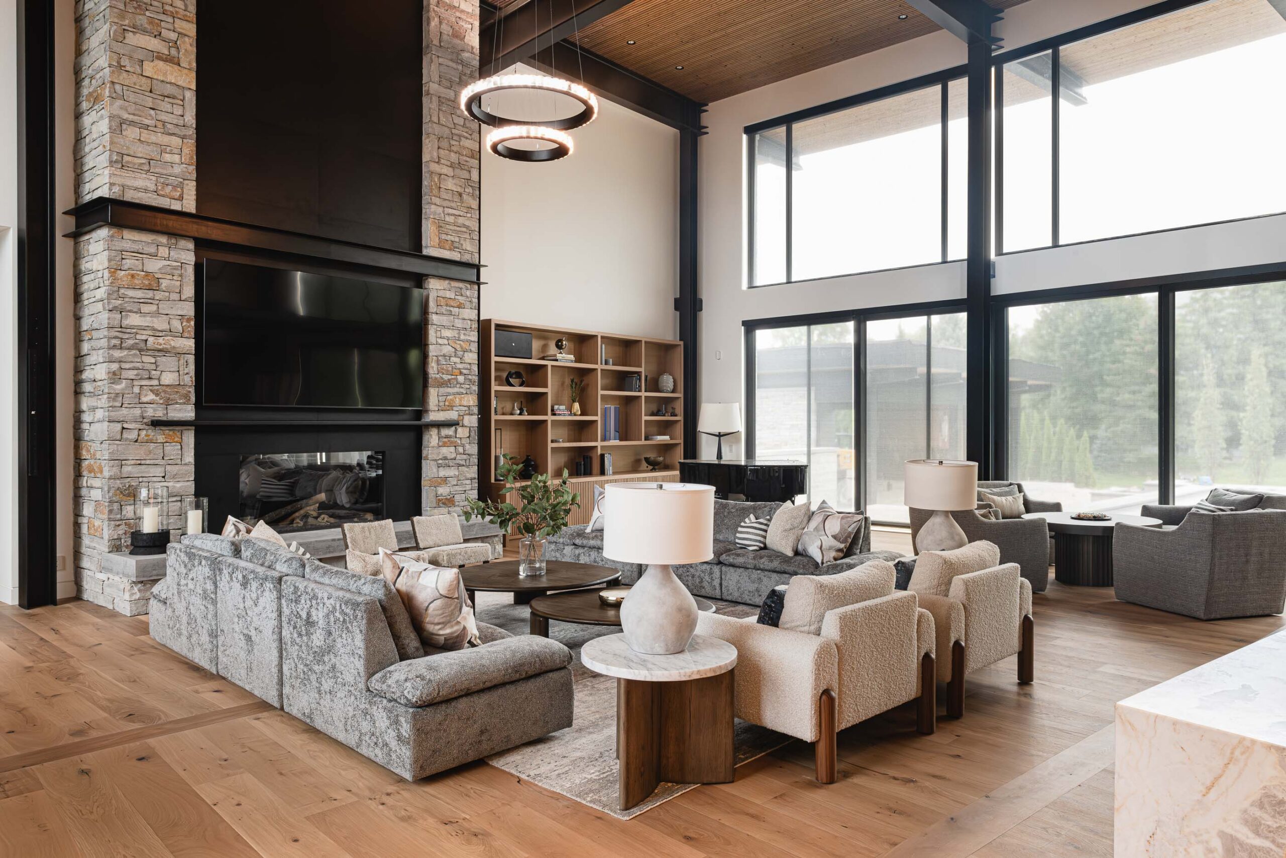 Great room in a contemporary chalet with distinct seating areas, industrial metal detailing, and two-storey stone fireplace