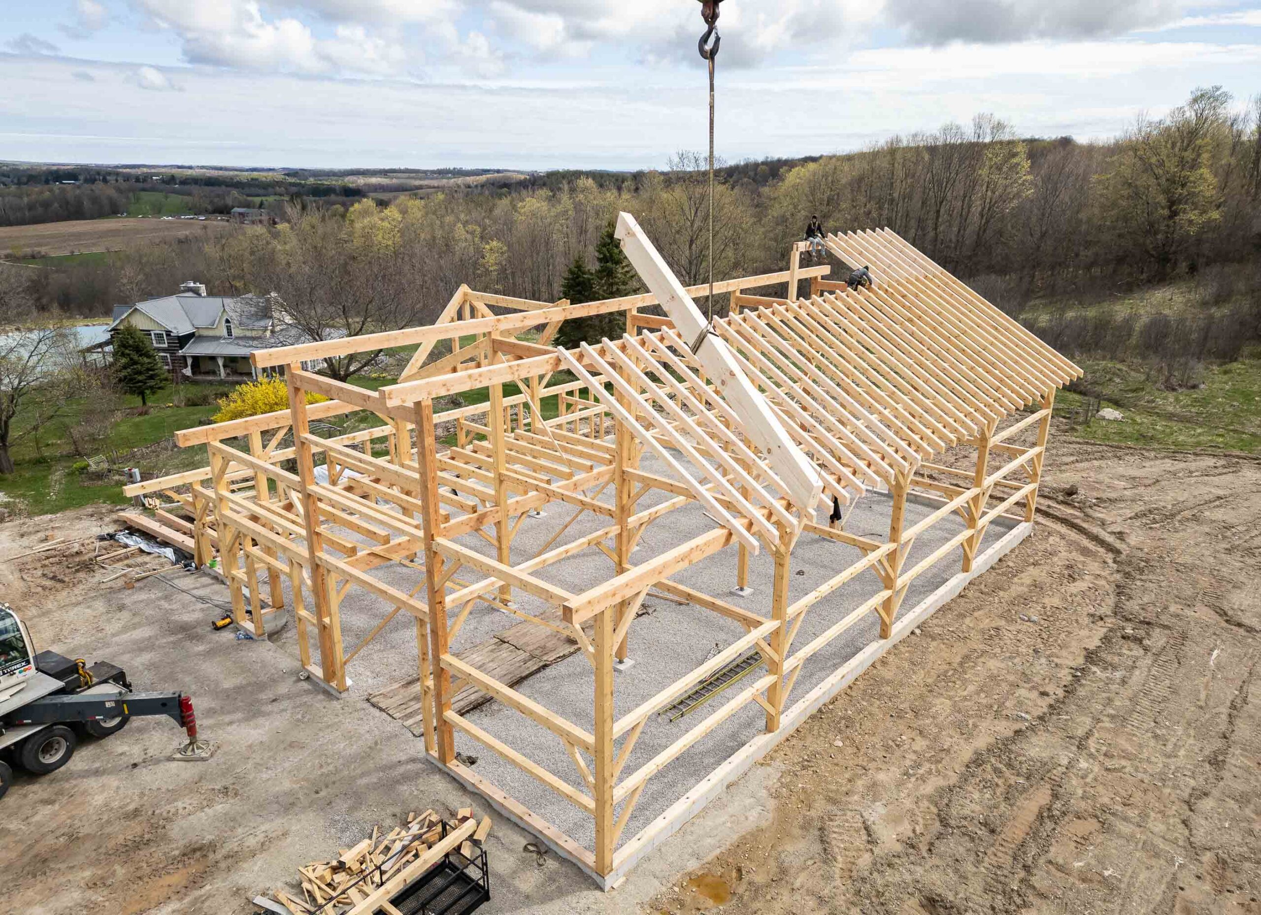 aerial view of roof joists being craned to workers building a timber frame barn with traditional techniques