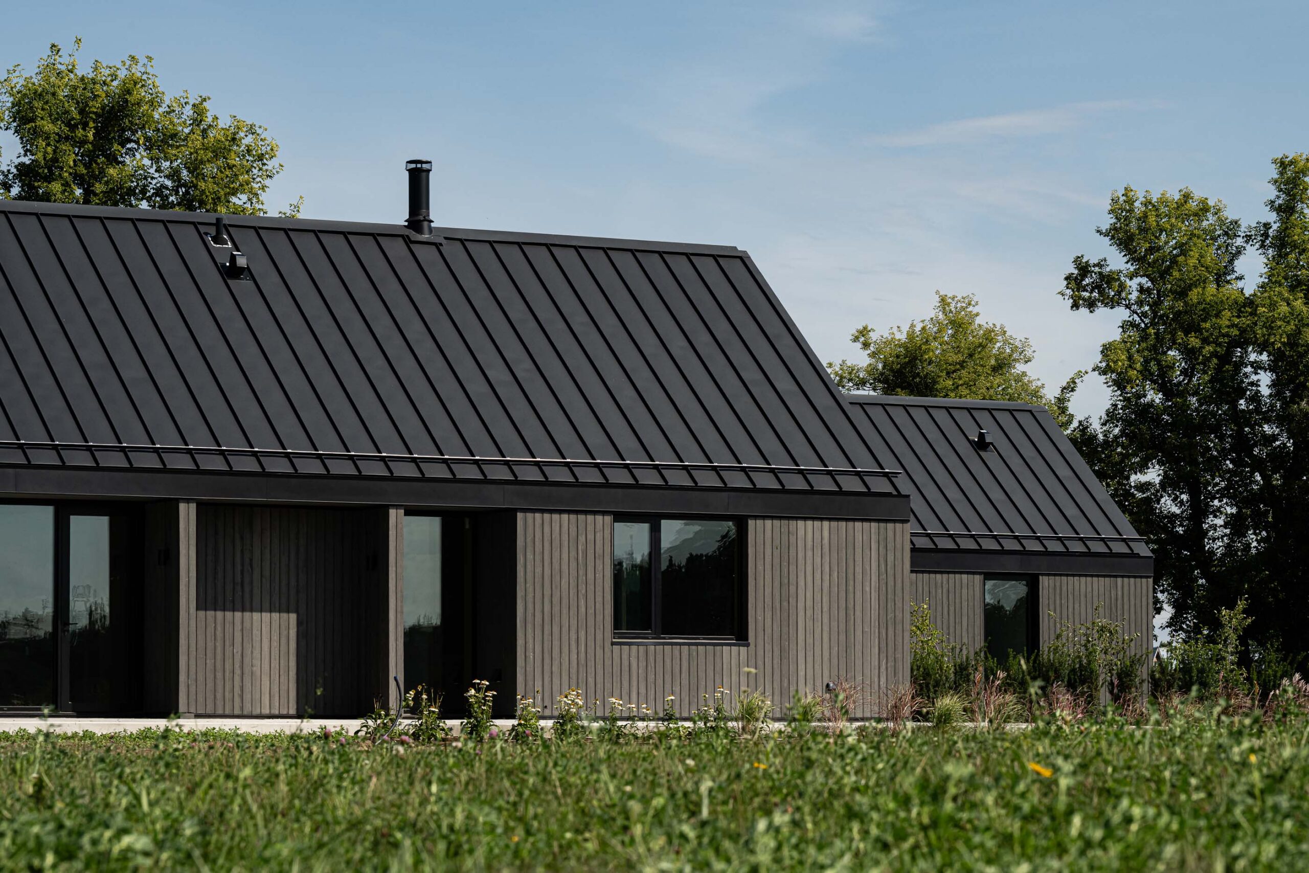 side elevation detail of a modern barn with two wings, contemporary vertical wood siding in dark grey and metal roof