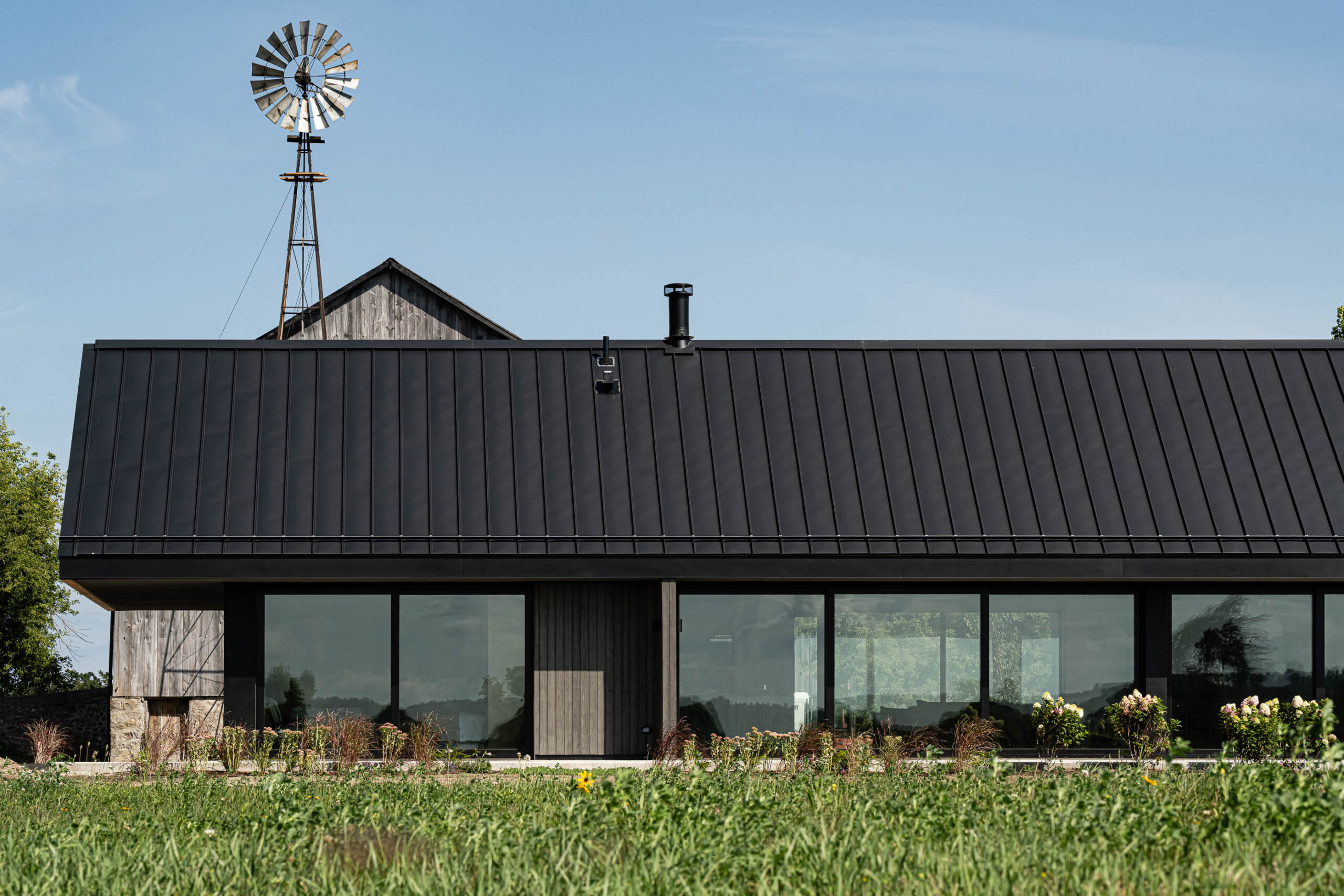 side elelvation of a modern barn build with floor to ceiling windows, oversized sliding doors, and contemporary details with a rustic barn in the background