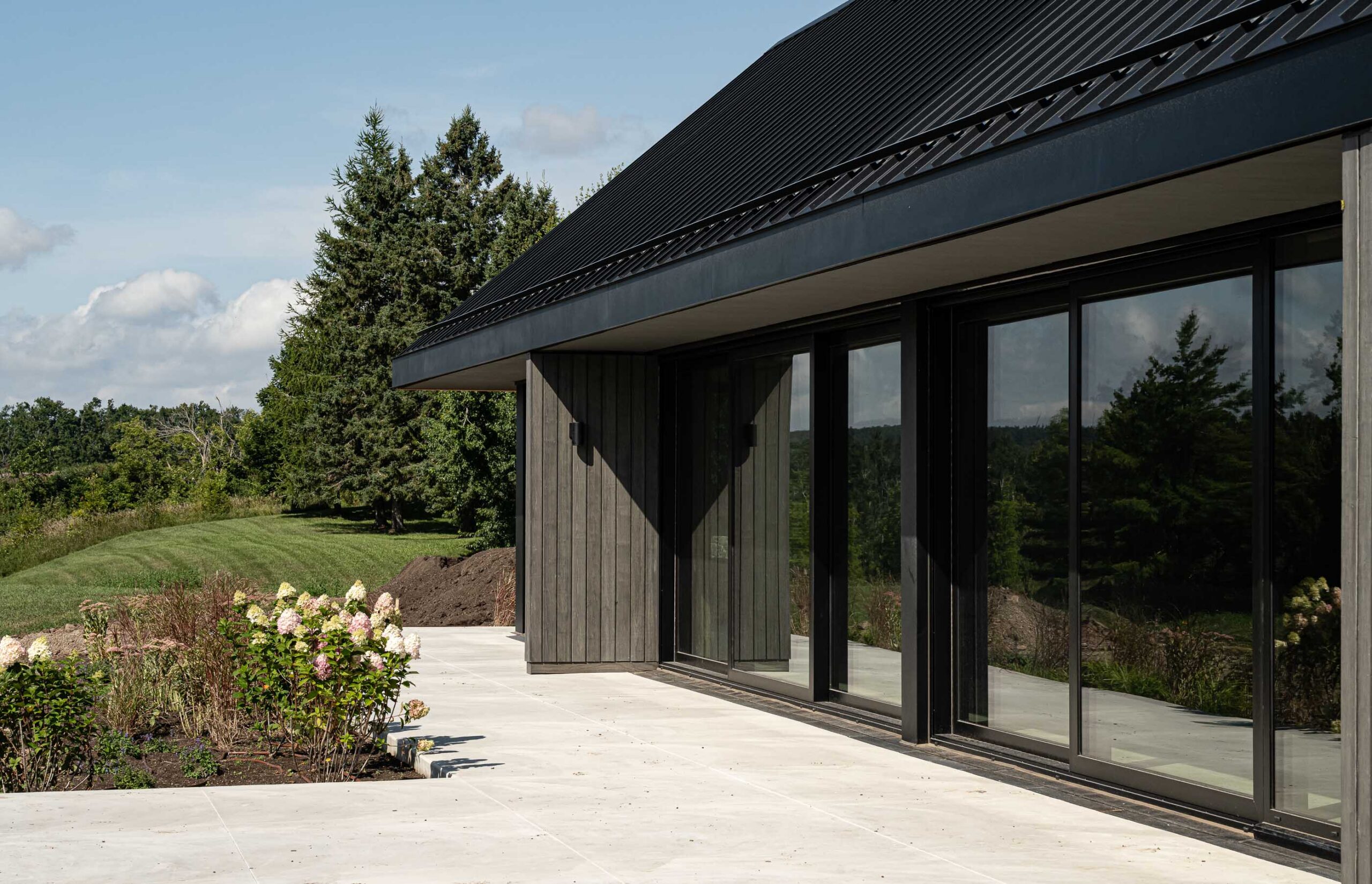 Side detail of a modern barn with extensive floor to ceiling glazing, contemporary wood siding and landscaping in progress