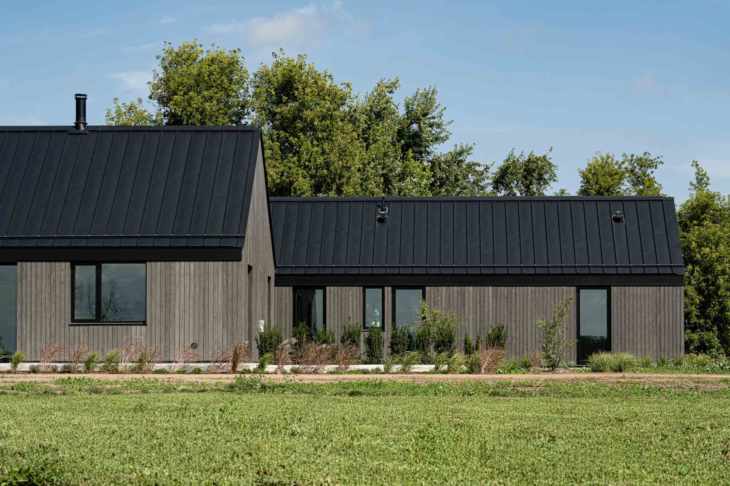 Side elevation detail of a Scandi-style modern barn home with contemporary metal roof, vertical wood siding detail and modern black framed windows