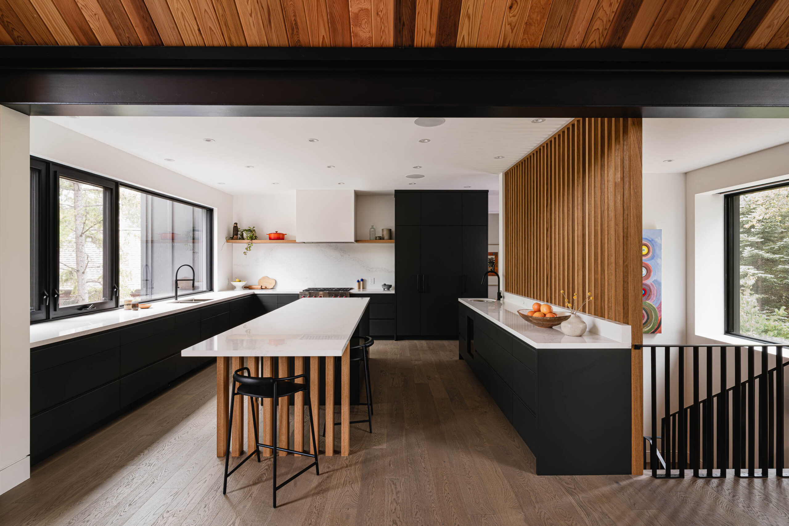 Contemporary kitchen in a Nordic-inspired alpine chalet with exposed structural steel beam, slatted wood wall, and expansive windows