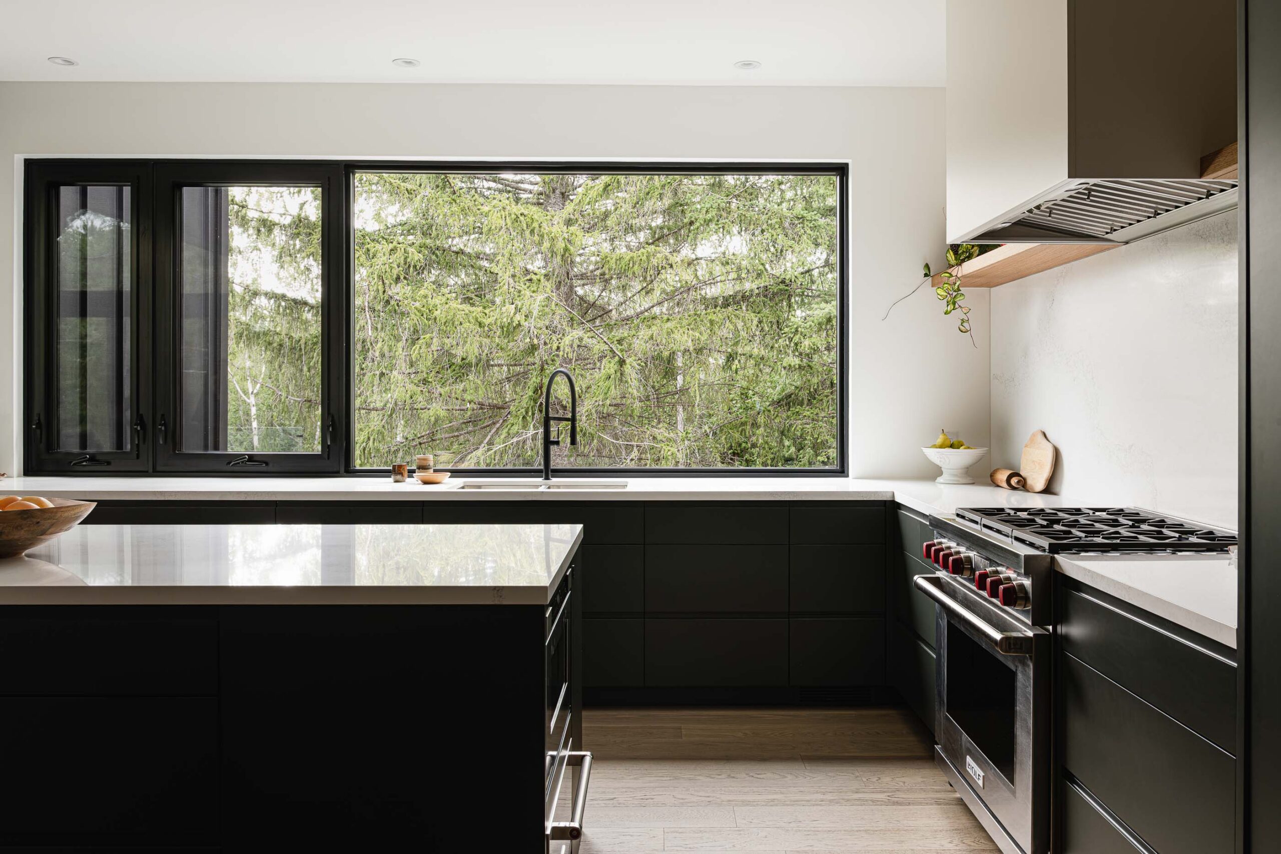 Contemporary kitchen with modern black cabinets, quartz counter and backsplash and expansive windows with forested views