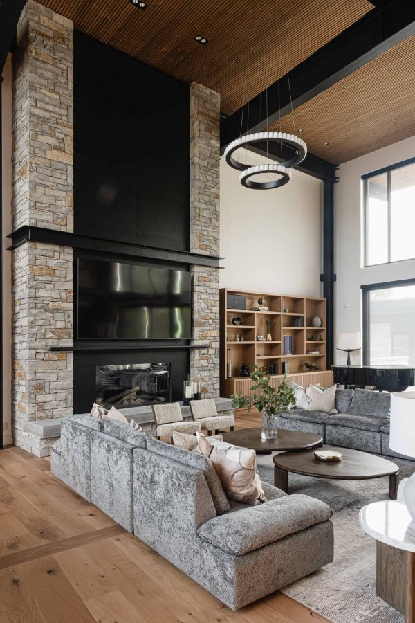 Great room in a contemporary chalet with distinct seating areas, industrial metal detailing, and two-storey stone fireplace
