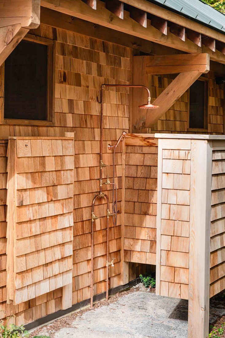 detail of an outdoor shower beside a cedar shake pool house with brass fixtures