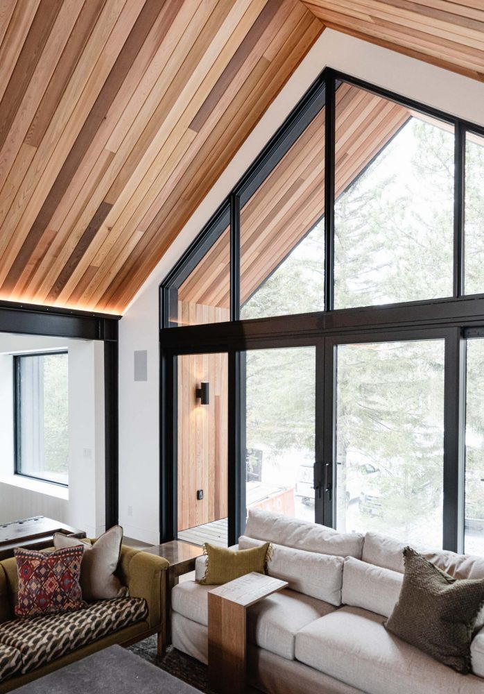 Contemporary alpine-inspired ski chalet with vaulted wood ceiling, steel beam accents, and modern, black frame windows and patio doors