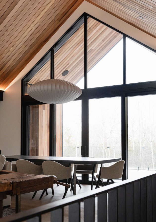 Modern alpine-inspired ski chalet with vaulted wood ceiling, black framed floor-to-ceiling windows, and contemporary lines.