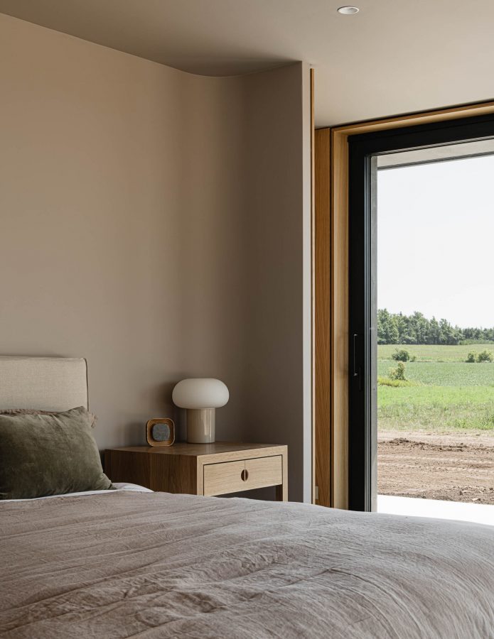 Detail of a contemporary bedroom with curved headboard wall, and floor to ceiling sliding doors overlooking surrounding landscape
