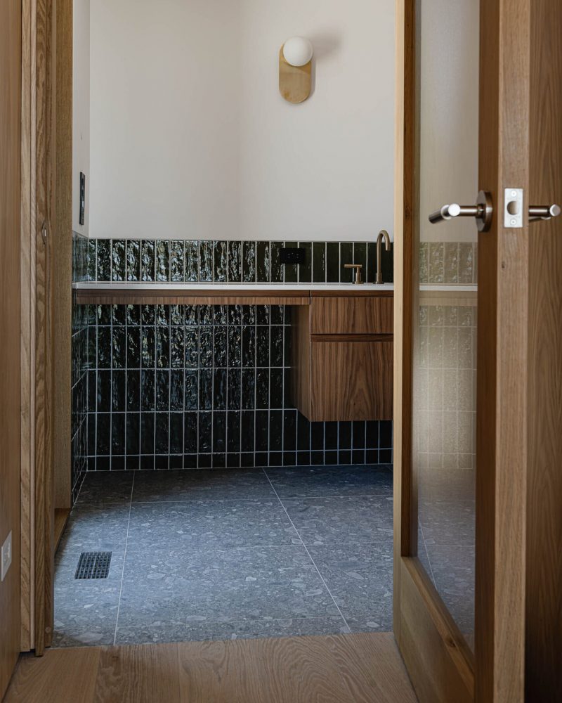reveal of a modern bathroom in construction with custom walnut vanity, oversized floor tile and rich green tile