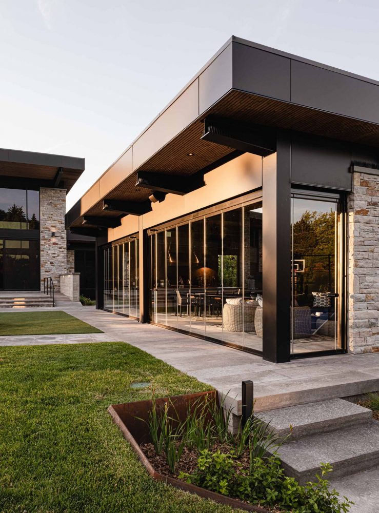 Custom-built luxury pool house with retractable glass walls, stone facade and modern cladding captured at dusk