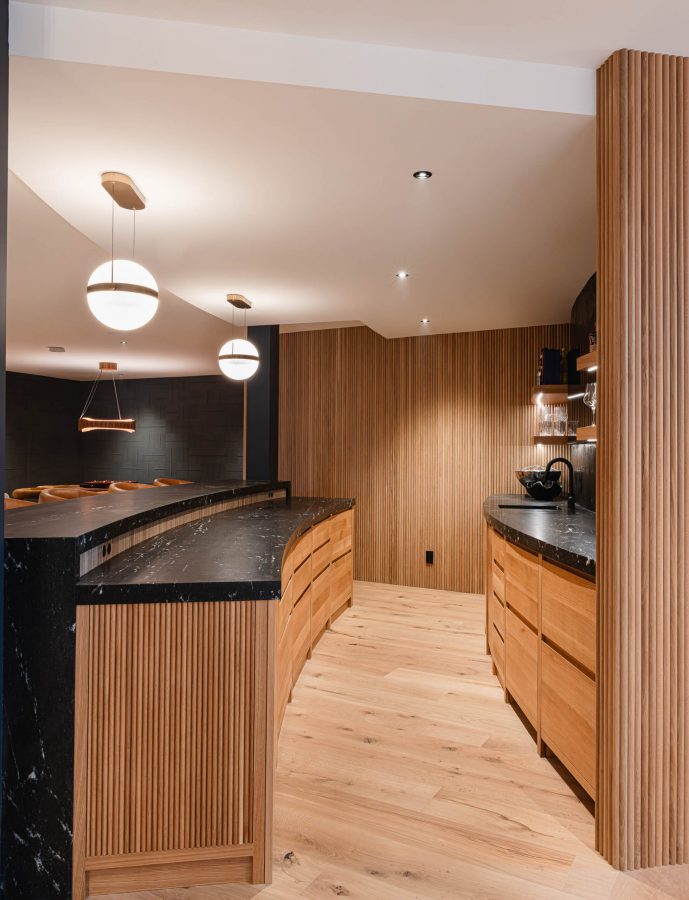 Curved custom home bar with dark quartz countertops, fluted wood paneling, and modern contemporary finishes