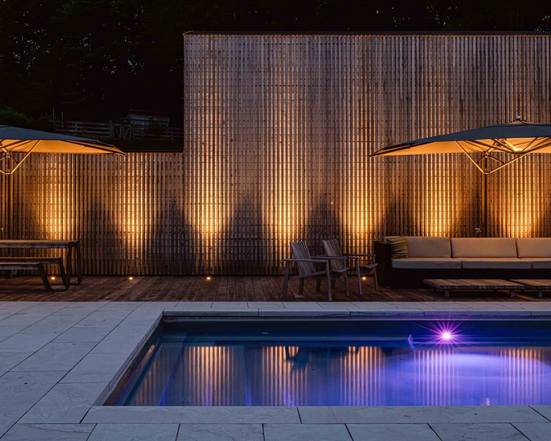 a modern pool lit up at night with vertical columns of light shining up a slat wall