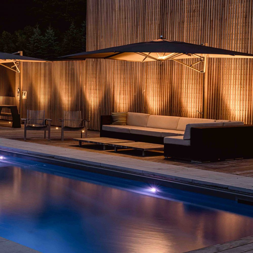 a modern pool lit up at night with vertical columns of light shining up a slat wall