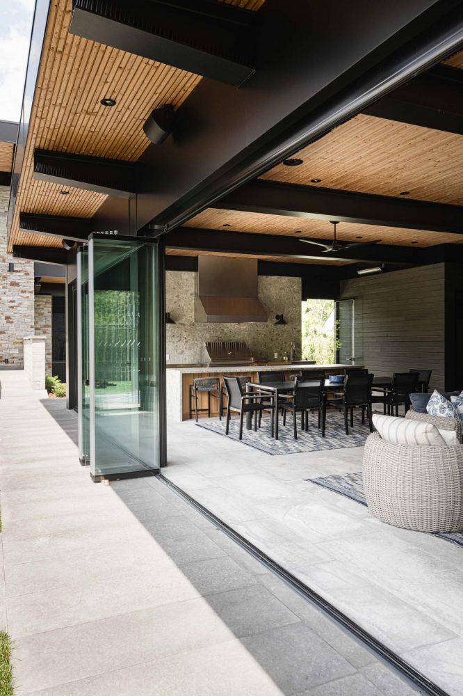 Modern Blue Mountain custom pool house with open retractable glass walls connecting indoor living and dining spaces to the outdoor entertaining areas