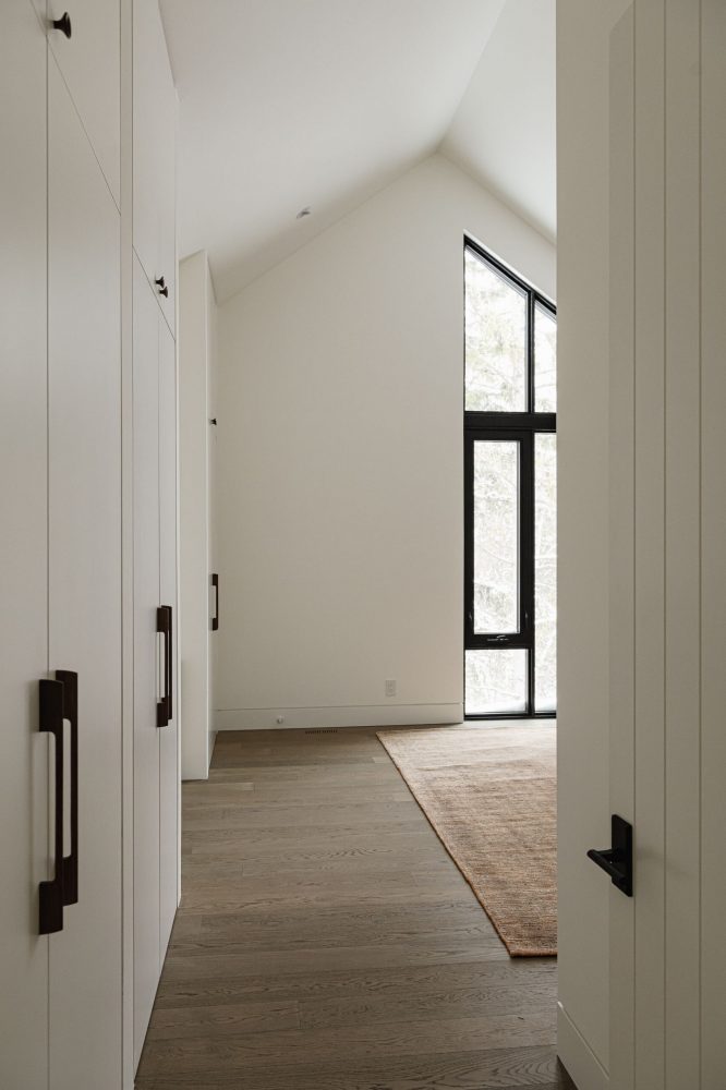 Contemporary Blue Mountain chalet bedroom detail with custom floor to ceiling cabinets, wide-plank wood flooring, and angular black-framed windows