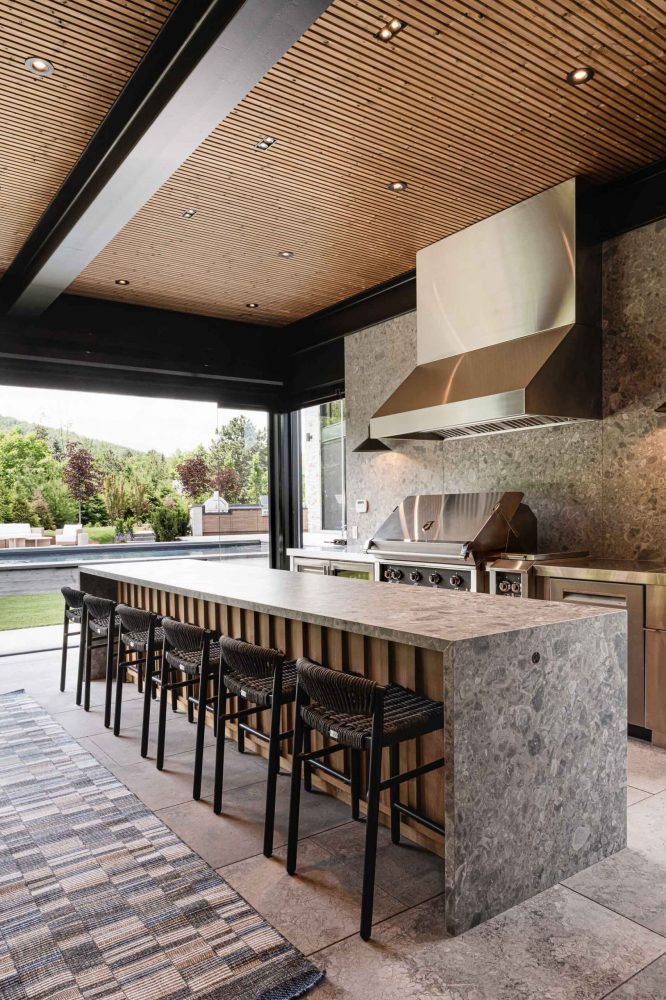 Modern Collingwood pool house kitchen with waterfall quartz island with bar seating, and floor to ceiling retractable glass walls open to the pool and outdoor living areas