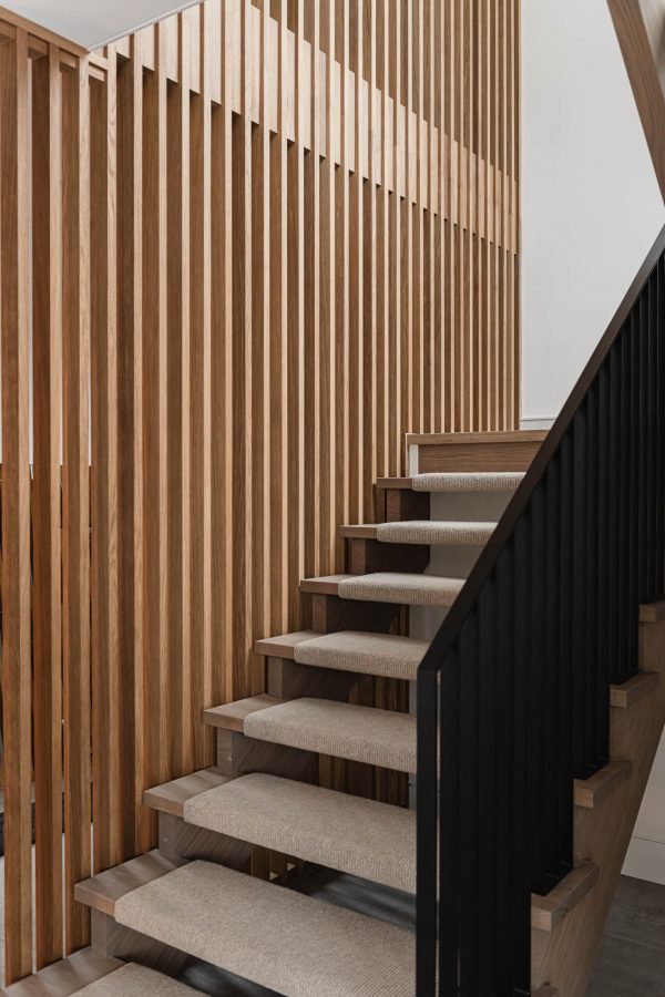 Modern chalet staircase detail with slotted wood wall, black metal railing and upholstered open-wood treads