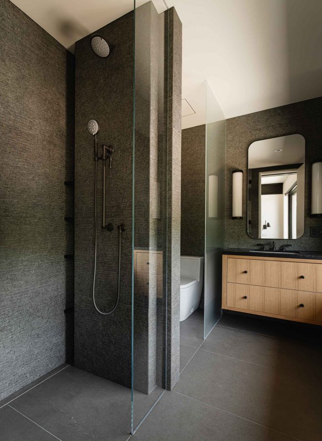 Dramatic modern Blue Mountain chalet bathroom with dark, textured tile shower, glass walled toilet room and floating vanity