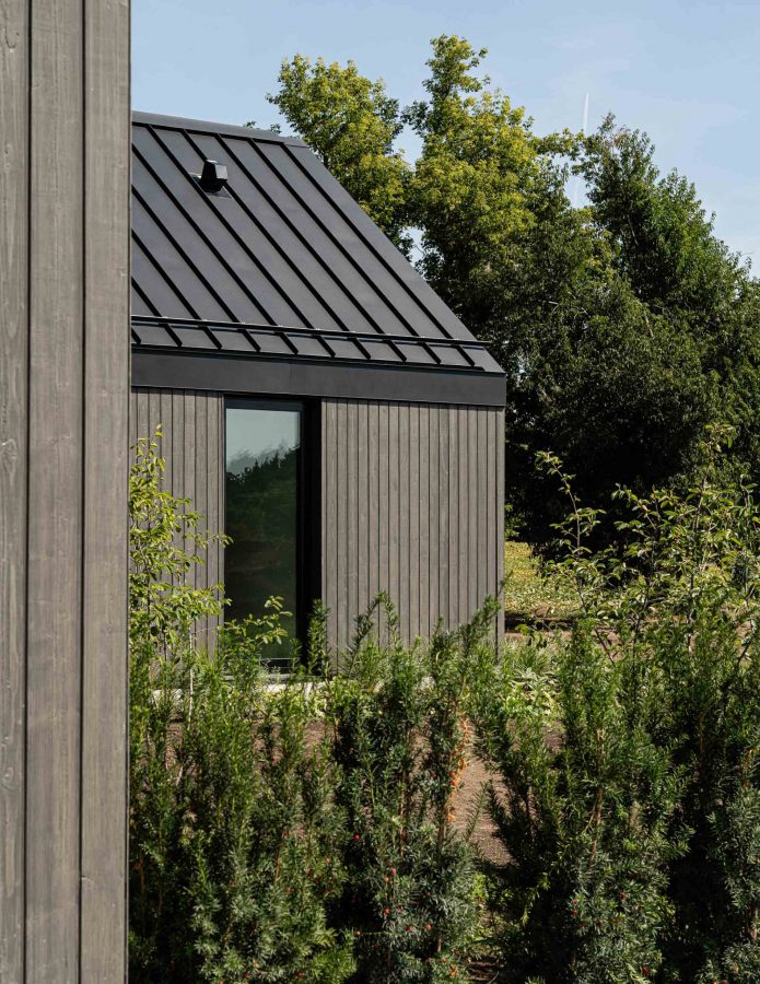 Detail of a SCandinavian-style modern barn with metal roof detailing, dark vertical wood siding and landscaping in progress
