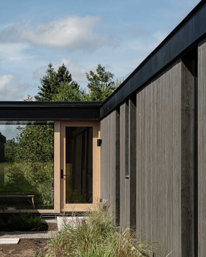 Side door detail of a modern barn in construction, with landscaping in progress, contemporary wood detailing, and sight lines through to the other side of the home