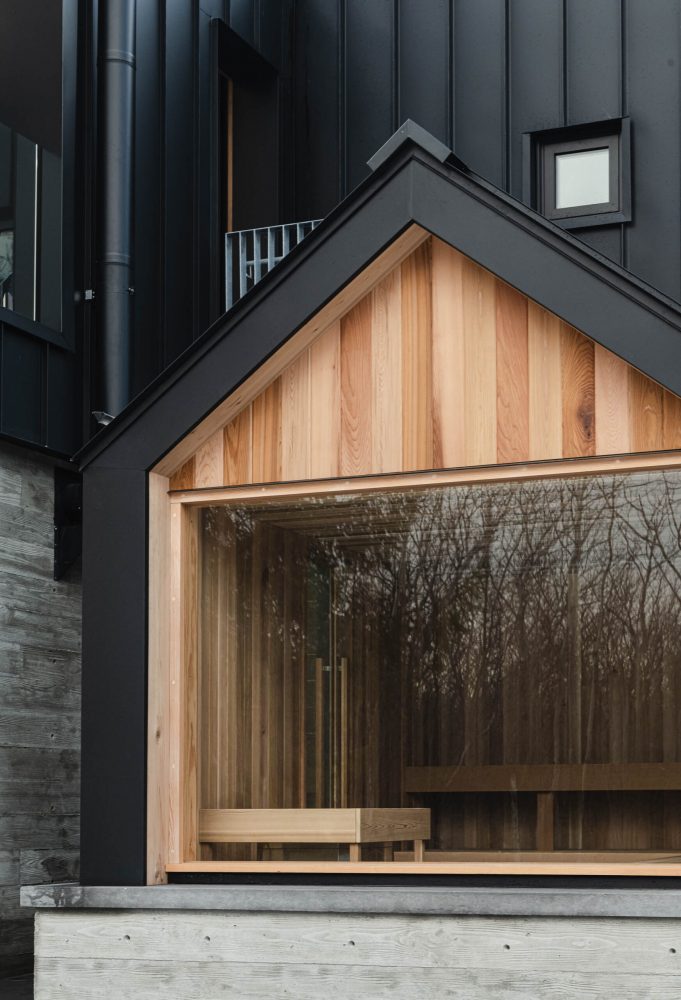 Modern Nordic-inspired glass-fronted sauna detail with board-formed concrete wall, black siding and rich wood accents