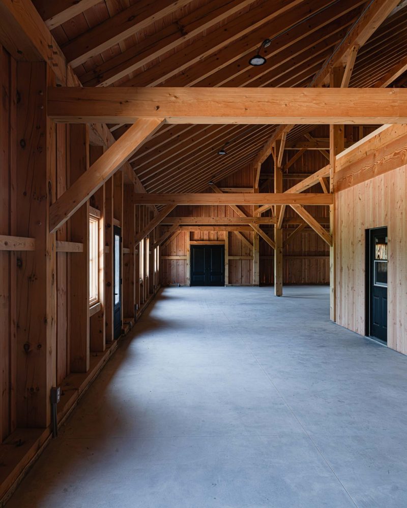 Interior detail of a timber frame barn with exposed beams, modern windows and polished concrete floors