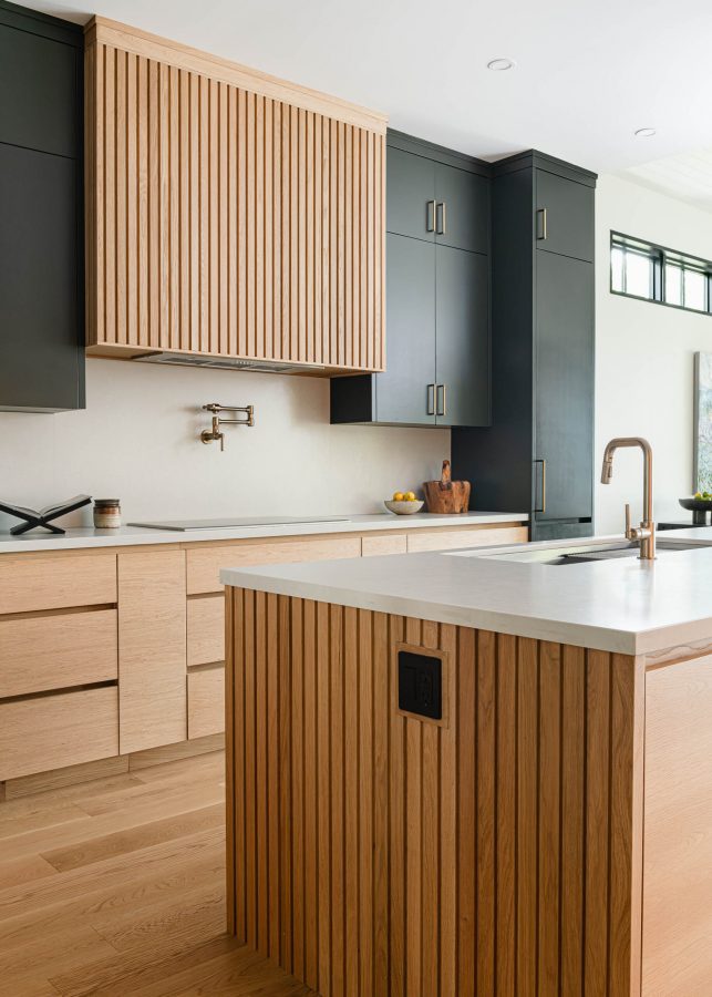 Contemporary kitchen in a custom built beach house with fluted wood detailing, quartz counter and backsplash, and sleek charcoal custom cabinetry