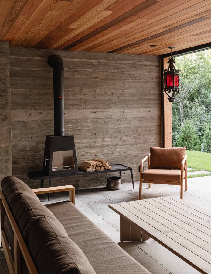 Nordic-inspired, covered outdoor seating area board formed concrete walls, retractable screens and a Scandinavia Stuv fireplace