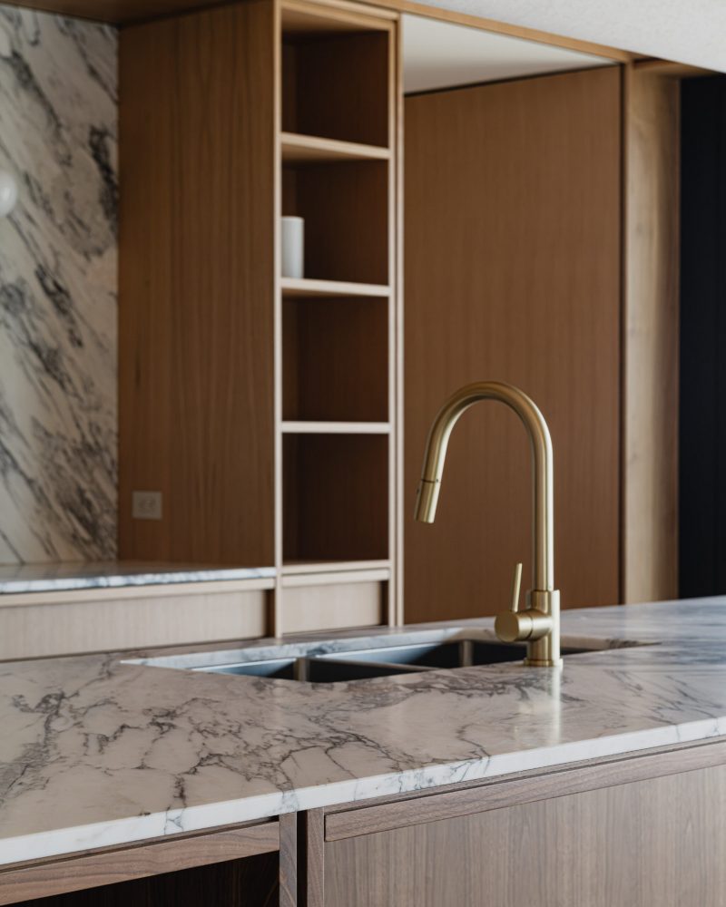 Kitchen island detail in a contemporary country kitchen with brass fixtures, walnut millwork and richly veined quartz countertop and backsplash