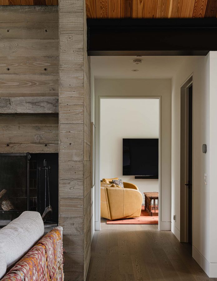 Board formed concrete fireplace detail in a modern alpine chalet, with view down the corridor into the media room