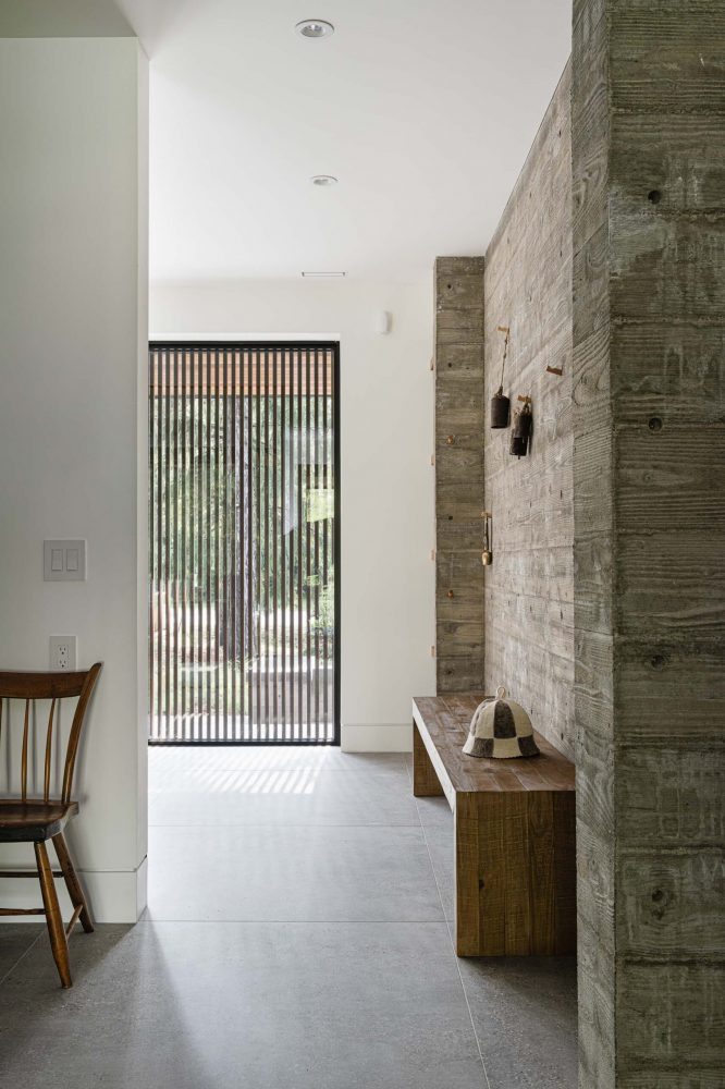 Board formed concrete accent wall in a modern alpine chalet, looking towards the front entry window with slat wood privacy screen