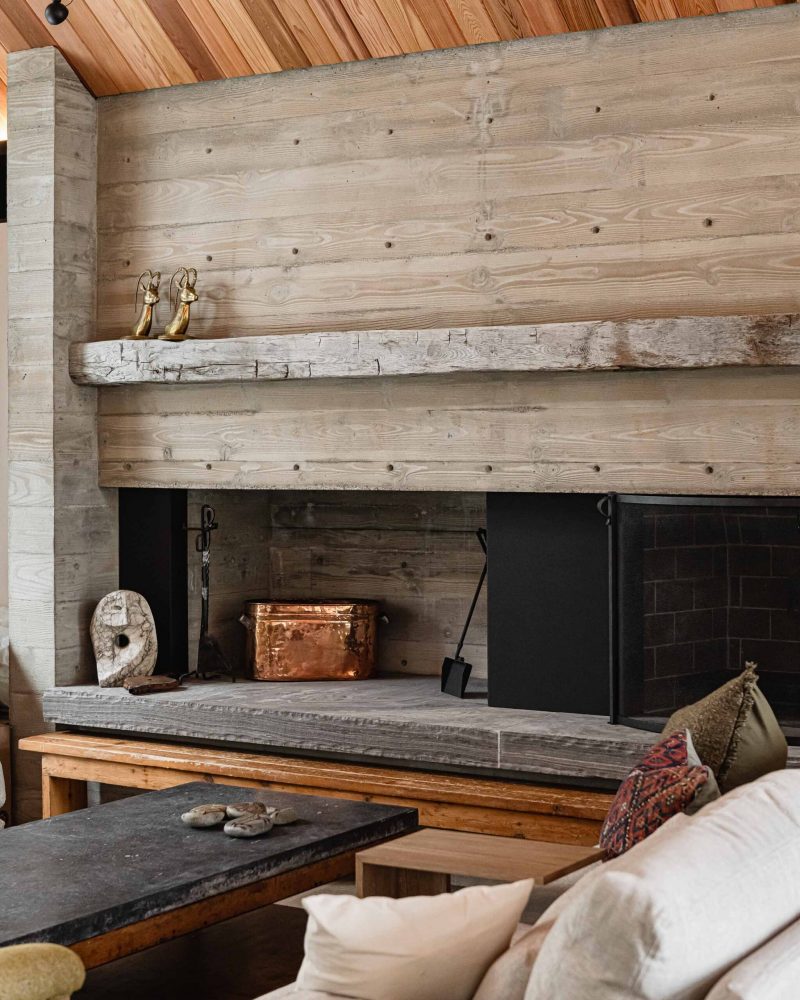 Detail of a board formed concrete fireplace with reclaimed timber mantle in a modern Blue Mountain chalet