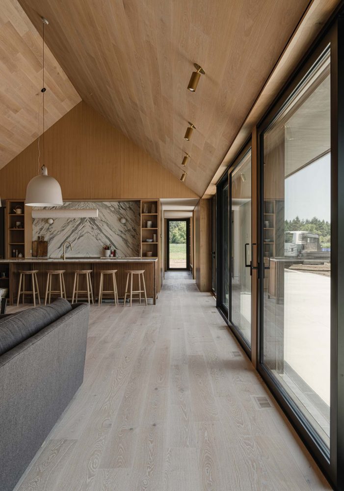 view along the floor-to-ceiling glazed wall spanning the kitchen, dining and living rooms of a modern barn build