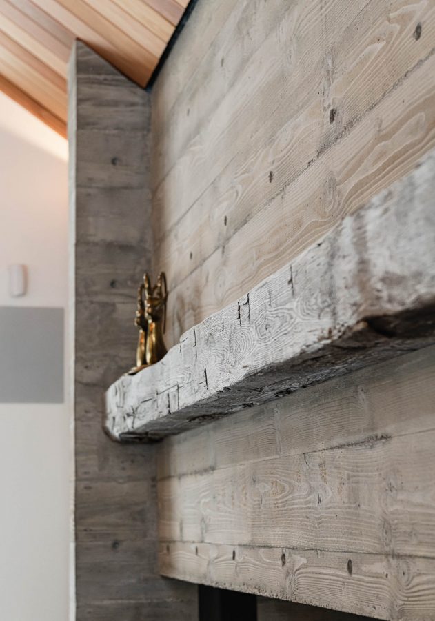 Detail of a board formed concrete fireplace with reclaimed timber mantle in a modern Blue Mountain chalet